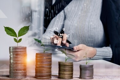 double exposure of businesswoman hand doing finances with tablet and tree piles of coins with small trees.