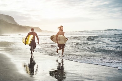 multigeneration friends going to surf on tropical beach - family people having fun doing extreme sport - joyful elderly and healthy lifestyle concept - main focus on young guy face