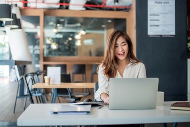 happy young asian businesswoman sitting on her workplace in the office. young woman working at laptop in the office.