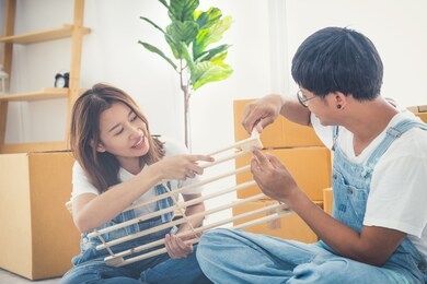young asian couple installing furniture in new house with instruction. couple putting together self assembly furniture in new home