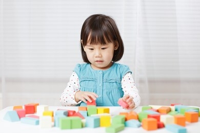 toddler girl playing creative toy blocks at home against white background