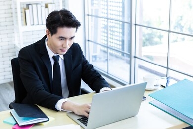 happy of asian young businessman see a successful business plan on the laptop computer and pen on wooden table background in office,business expressed confidence embolden