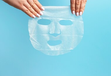 female hands with white manicure hold fabric mask on a blue background.
