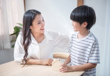 asian son hand coin on mother palm with saving house shape container,happiness family mom and child invest for education planning finance in livingroom at home.