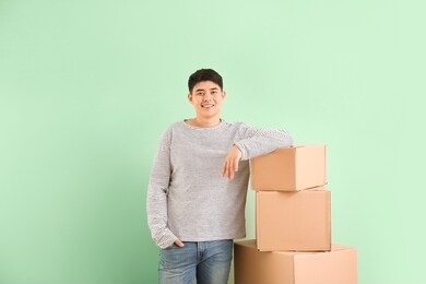asian man with moving boxes on color background