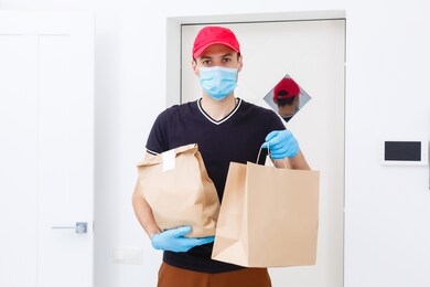 delivery man holding paper bag with food on white background, food delivery man in protective mask and protective gloves