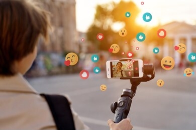 teen girl blogger vlogger record vlog streaming video hold phone on selfie stick in urban city. young female vlogger shoot social media blog on smartphone get likes emoji, over shoulder closeup view.