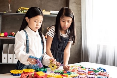 two little girl playing colorful lego on desk with interested feeling.at home studio.blurry light around