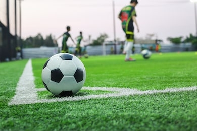 the football ball is placed in the corner of a small football field. and on the back there is a child rehearsing the ball on the training field used as an illustration