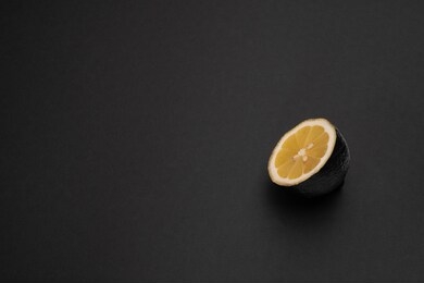 one half of black lemon on the matte black background. the object is at the right side of the picture. minimal style. conceptual minimalism. matte surface. sliced fruit. one. copy space