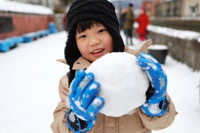 cute asian child playing on snow in the park.