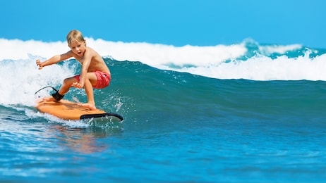 happy baby boy - young surfer learn to ride on surfboard with fun on sea waves. 