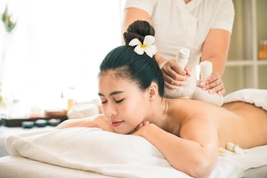 spa,wellness, beauty and relaxation concept -beautiful young asian woman lying on the bed having a massage with herbal compresses at beauty spa. thai massage for health.