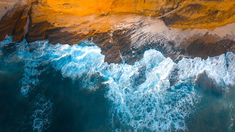 wonderful aerial photograph of a beach where the sea breaks into the stones. the blue of the pacific blends with the orange color of the beach stones.