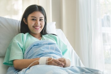 patient happy after ill and have a health insurance. young  asian girl lying on bed in hospital and feeling relaxed after recovery from emergency sick.