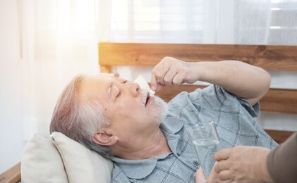 asian senior man taking medicines and drinking water while lie on couch at home, health and medicine concept with copy space.