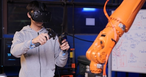 professional engineer is controlling a futuristic robotic arm with a virtual reality headset and joysticks in a high tech research laboratory with modern equipment.
