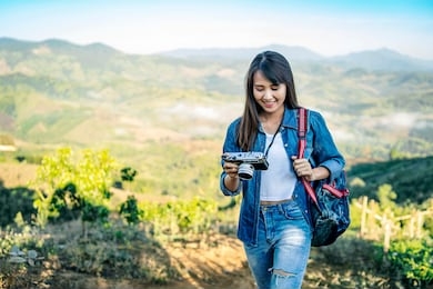 asian tourist traveler girl in an adventure traveling on the mountains, using a digital camera taking a photograph of the misty mountain view in the morning sunrise wearing a denon jacket and backpack