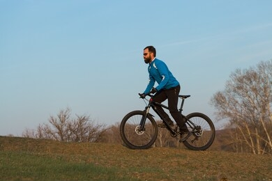 cyclist in pants and fleece jacket on a modern carbon hardtail bike with an air suspension fork. the guy on the top of the hill rides a bike.