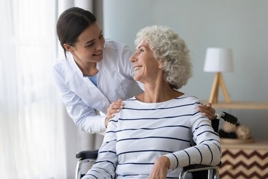 happy female nurse or caregiver talk support positive handicapped old lady patient sitting in wheelchair in hospital, young woman doctor give help take care of mature handicapped grandmother