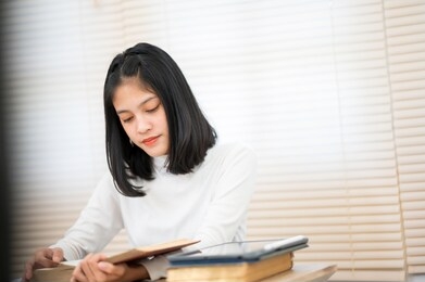 an asian female student wearing a white shirt sitting and reading at university