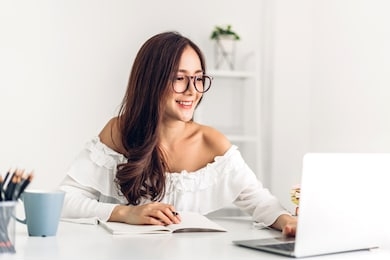 portrait of smiling happy beautiful asian woman relaxing using technology of laptop computer while sitting on table.young creative girl working and typing on keyboard at home.work at home concept