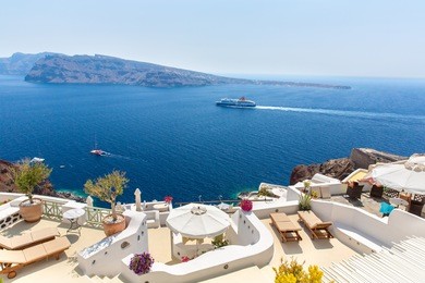 view of fira town - santorini island,crete,greece. white concrete staircases leading down to beautiful bay with clear blue sky and sea