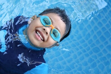 happy child playing in blue colour swimming pool. boy with swimming goggles. kid practice water sport. summer vacation concept.