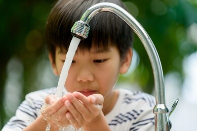 selective focus at boy hands taking water from modern faucet in home garden.