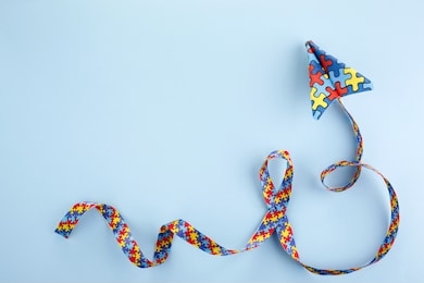autism awareness day or month. paper plane in origami style with autism awareness puzzle ribbon on blue background.
