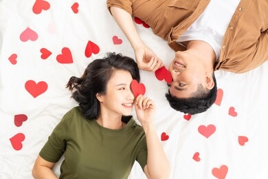 smiling young couple lying on bed with many heart shapes.