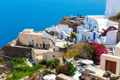 view of fira town - santorini island,crete,greece. white concrete staircases leading down to beautiful bay with clear blue sky and sea