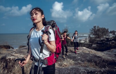 group of hikers walking in mountains. young happy travelers hiking with backpacks on the beautiful rocky trail at warm sunny evening. trek hiking destination experience lifestyle concept