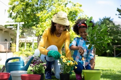 front view of an african american woman and her daugther in the garden, kneeling and potting plants. family enjoying time at home, lifestyle concept