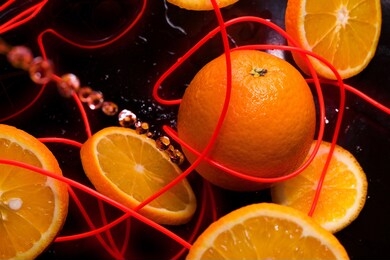 oranges on a black background with a neon ribbon and sunglasses.