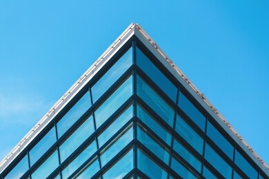 triangular corner of a glass building against a blue sky. minimalistic architecture. toned
