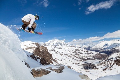 jumping snowboarder keeps one hand on the snowboard on blue sky background