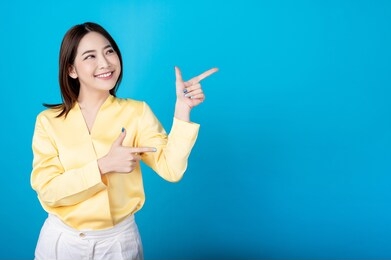 beautiful young asian woman presenting point to copy space with big smile happy beaming face in seamless blue  isolated background. presenter promotion, happy lifestyle, fresh pretty girl concept.