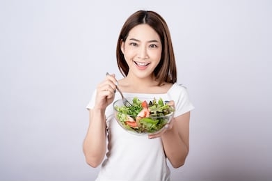 beautiful young asian eating salad with big smile happy beaming face in seamless white  isolated background. diet healthy concept. her face and skin are healthy, fresh, bright and youthful.