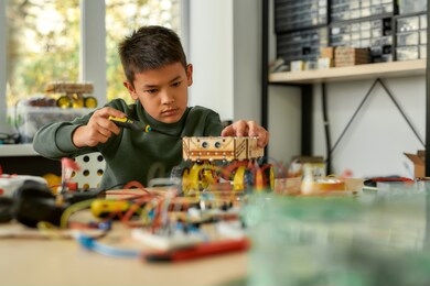 boy using screwdriver while fixing bolts on a robot vehicle. smart kids and stem education. robotics and software engineering for elementary students. selective focus