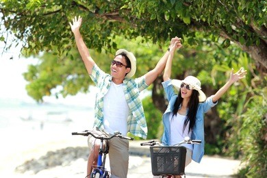 man and woman having fun outdoor riding bicycle together and smiling to the camera