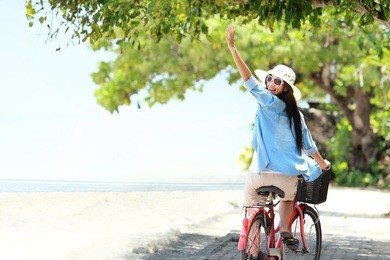 carefree woman having fun riding bicycle and raised her arm at the beach
