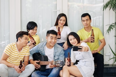 pretty smiling young asian woman taking selfie with friend playing guitar at house party