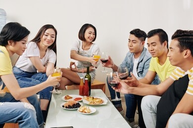 group of vietnamese young people talking, having drinks and food at house party
