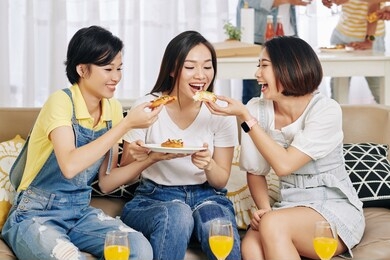 laughing happy female friends sharing small pizza at house party