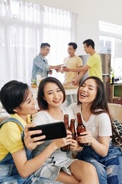 pretty smiling female friends taking group selfie at house party