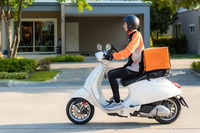 asian man courier on scooter delivering food in town streets with a hot food delivery from take aways and restaurants to home, express food delivery and shopping online concept.