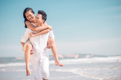 close up image of a young funny couple piggybacking on the beach 