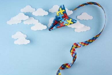 autism awareness day or month. paper plane in origami style with autism awareness puzzle ribbon on blue background.