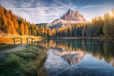 lake with reflection in mountains at sunrise in autumn in dolomites, italy. landscape with antorno lake, small wooden bridge, trees with orange leaves, high rocks, blue sky in fall. colorful forest 